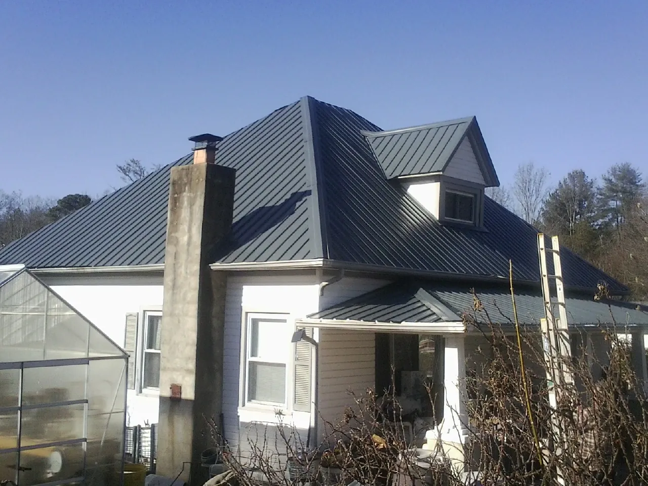 Dark blue standing seam metal roof on a white farmhouse with dormer — Slate & Tile Roof Repair by Roofing Brothers in Almont