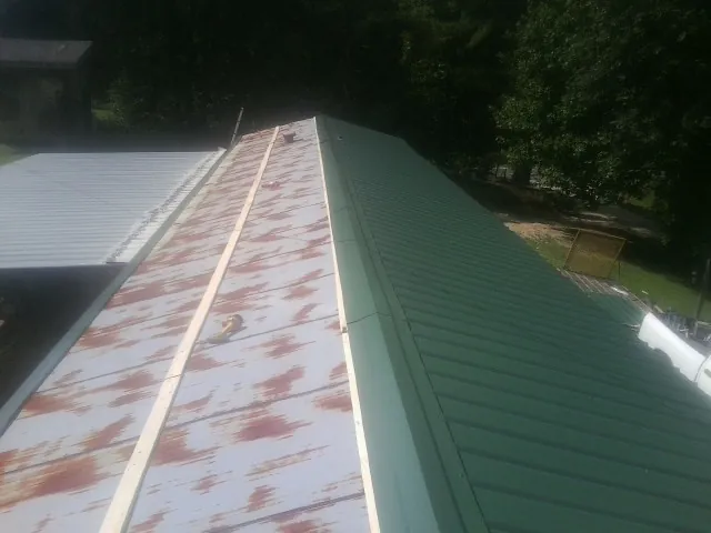 Old rusted panels beside newly installed green metal roofing — Wind Damage Roof Repair by Roofing Brothers in Almont