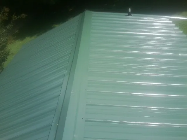 New green metal panels meeting at the ridge of a roof — Flat Roof Repair work by our crew in Almont