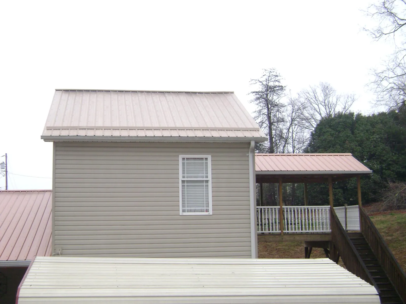 Tan metal roofs on a two story addition and attached porch, from a Roof Replacement job in Almont